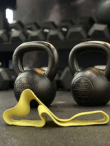 Two black kettlebells with a yellow resistance band on a gym floor.