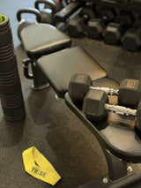 Dumbbells on a weight rack with a yellow 'TRIBE' band on a dark surface
