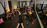 Group of people exercising in a gym with mirrors and fitness equipment.