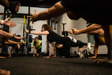 Group of people exercising in a gym setting with mirrors and fitness equipment.