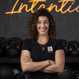 Woman standing with arms crossed in front of a black background with 'Intentions' written in neon lights.